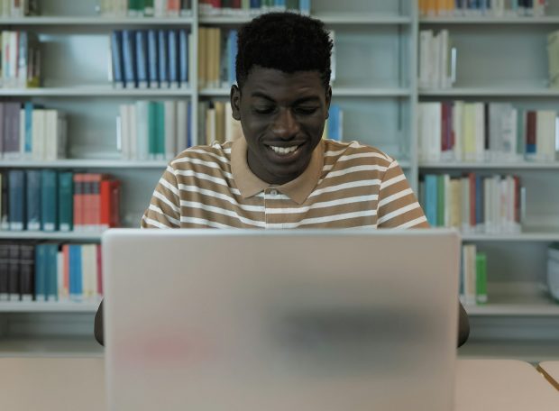 Young African student using laptop in library - School education concept